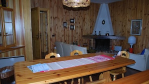 Een houten eettafel met een menukaart, omringd door houten stoelen, in een kamer met houten wanden en een open haard.