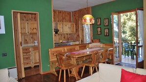 Een eetgedeelte met houten meubels, een keuken met houten kastjes en een uitzicht door een glazen deur.