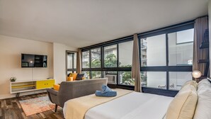 Ein modernes Hotelzimmer mit einem großen Bett, einem Schreibtisch, einem Fernseher und einem Fenster mit Blick auf Gebäude.