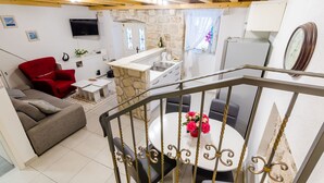Un salon avec un fauteuil rouge, un canapé gris, une table à manger avec des chaises, un coin cuisine avec un mur en pierre et un téléviseur fixé au mur.