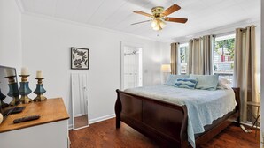 Un dormitorio con una cama de madera, un ventilador de techo, un escritorio con lámpara y una puerta que da a otra habitación.
