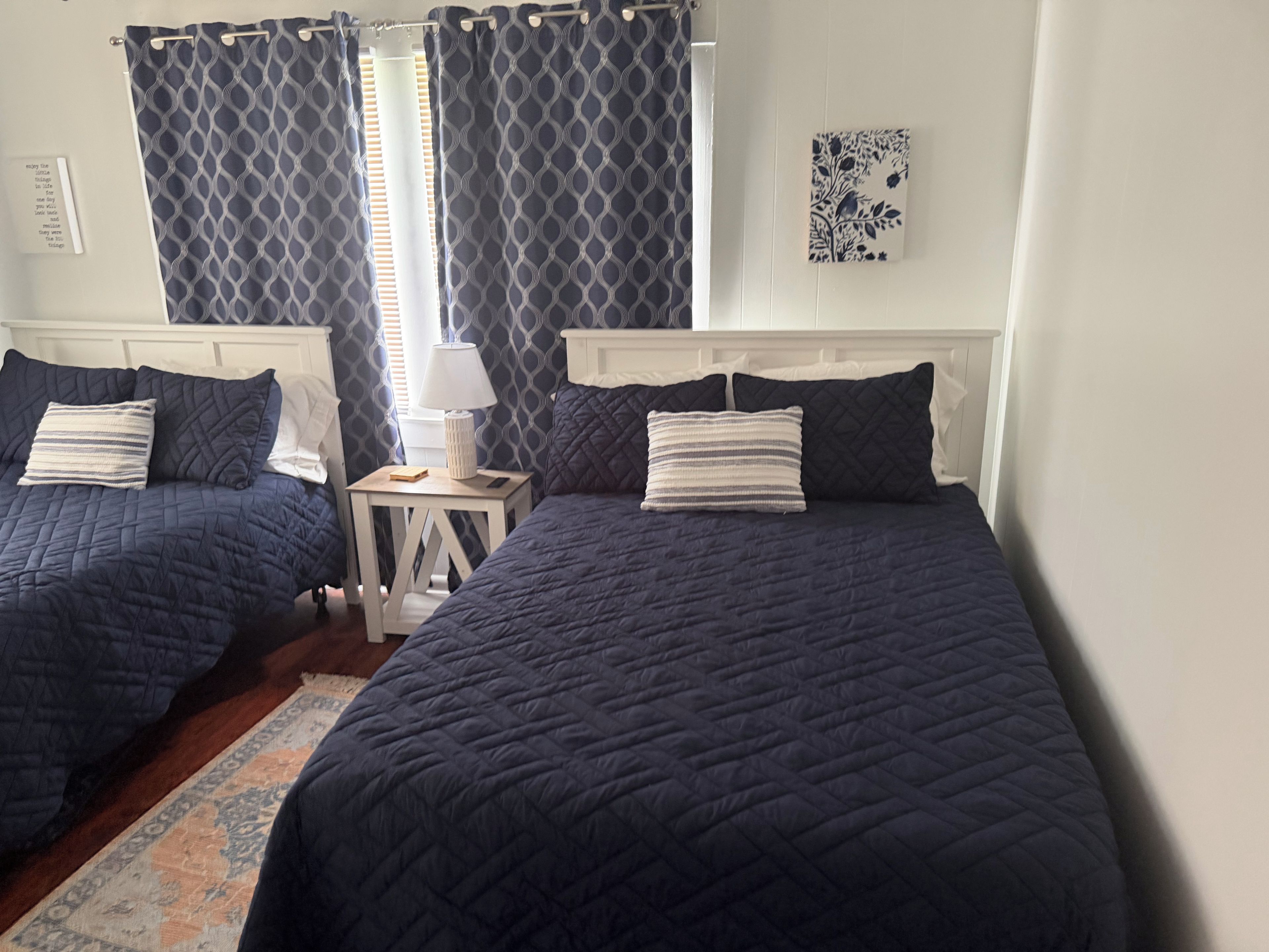 A room with two beds, a nightstand, a lamp, and a window with curtains.