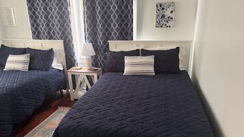 A room with two beds, a nightstand, a lamp, and a window with curtains.