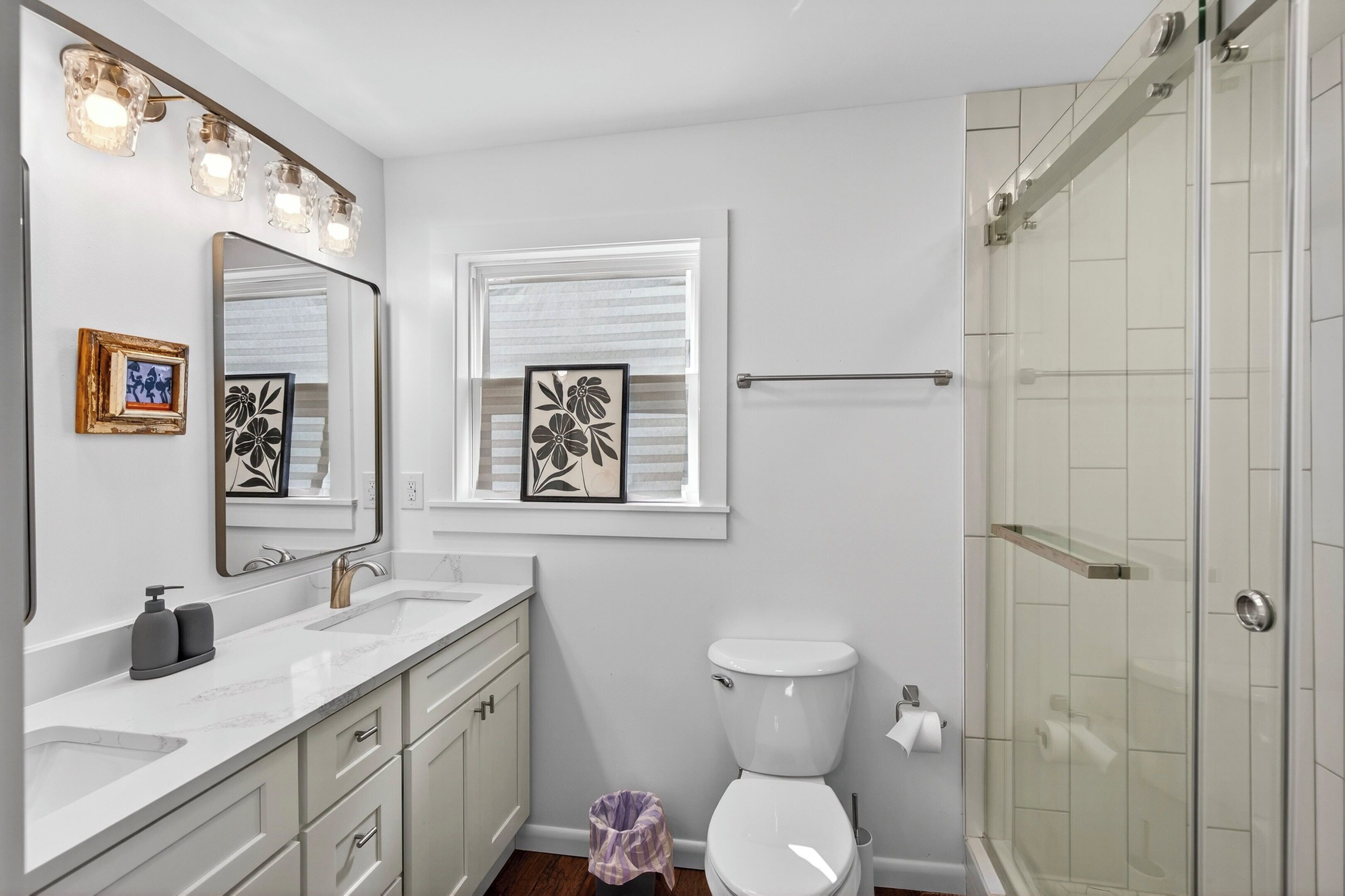 Une salle de bain avec des toilettes blanches, un lavabo avec un miroir et un espace douche.