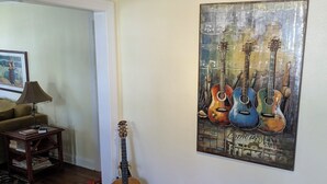 Una sala de estar con una guitarra, un cuadro de guitarras, una lámpara, un sofá y una mesa con libros y una cesta.