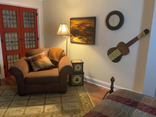 Una sala de estar acogedora con un sillón marrón, una lámpara, una decoración de guitarra en la pared y una mesita con un reloj.