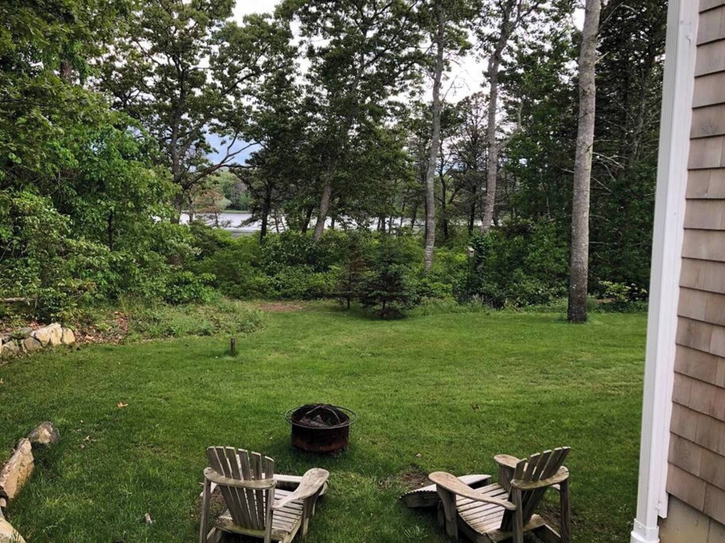A backyard with a fire pit, two Adirondack chairs, and a stone wall.
