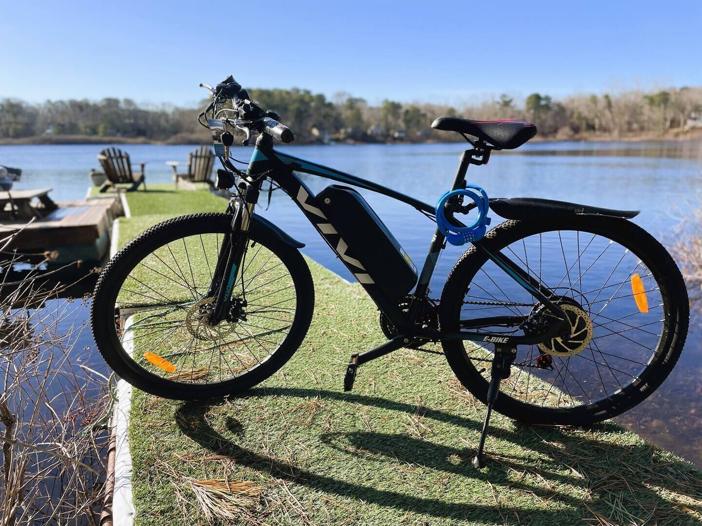 A stationary electric bike by a lakeside with a picnic table and chairs in the background.