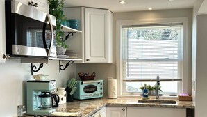 A kitchen with white cabinets, a black stove, a blue toaster, and a window with blinds.