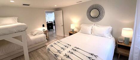 A bedroom with a large bed, two smaller beds, a round mirror, bedside lamps, and a door leading to another room.