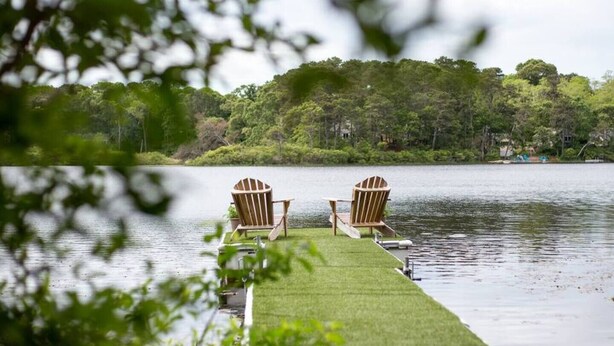 A lakeside deck with two Adirondack chairs and a small dock extending into the water.
