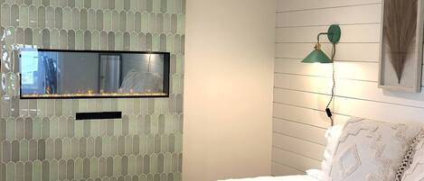 A bedroom with a bed, a mounted TV, a wall-mounted lamp, and a framed artwork.