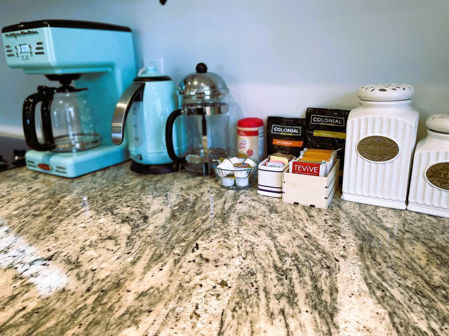 A kitchen counter with a coffee maker, a kettle, a teapot, and containers of coffee and tea.