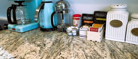 A kitchen counter with a coffee maker, a kettle, a teapot, and containers of coffee and tea.