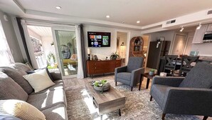 A modern living room with a sofa, armchairs, a coffee table, and a TV mounted on the wall.