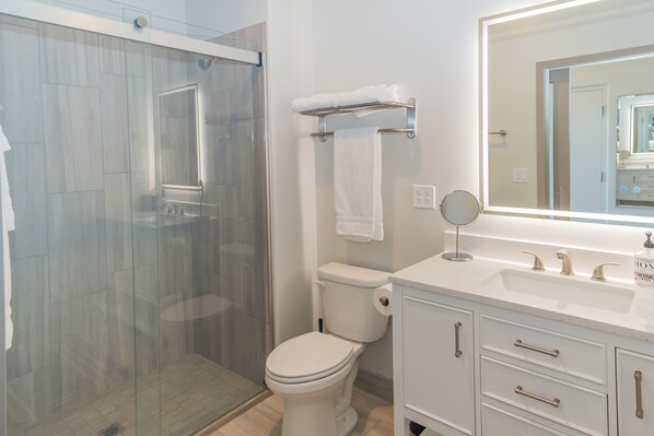 Une salle de bain moderne avec une douche à parois de verre, des toilettes blanches, un meuble-lavabo avec un miroir et un évier.