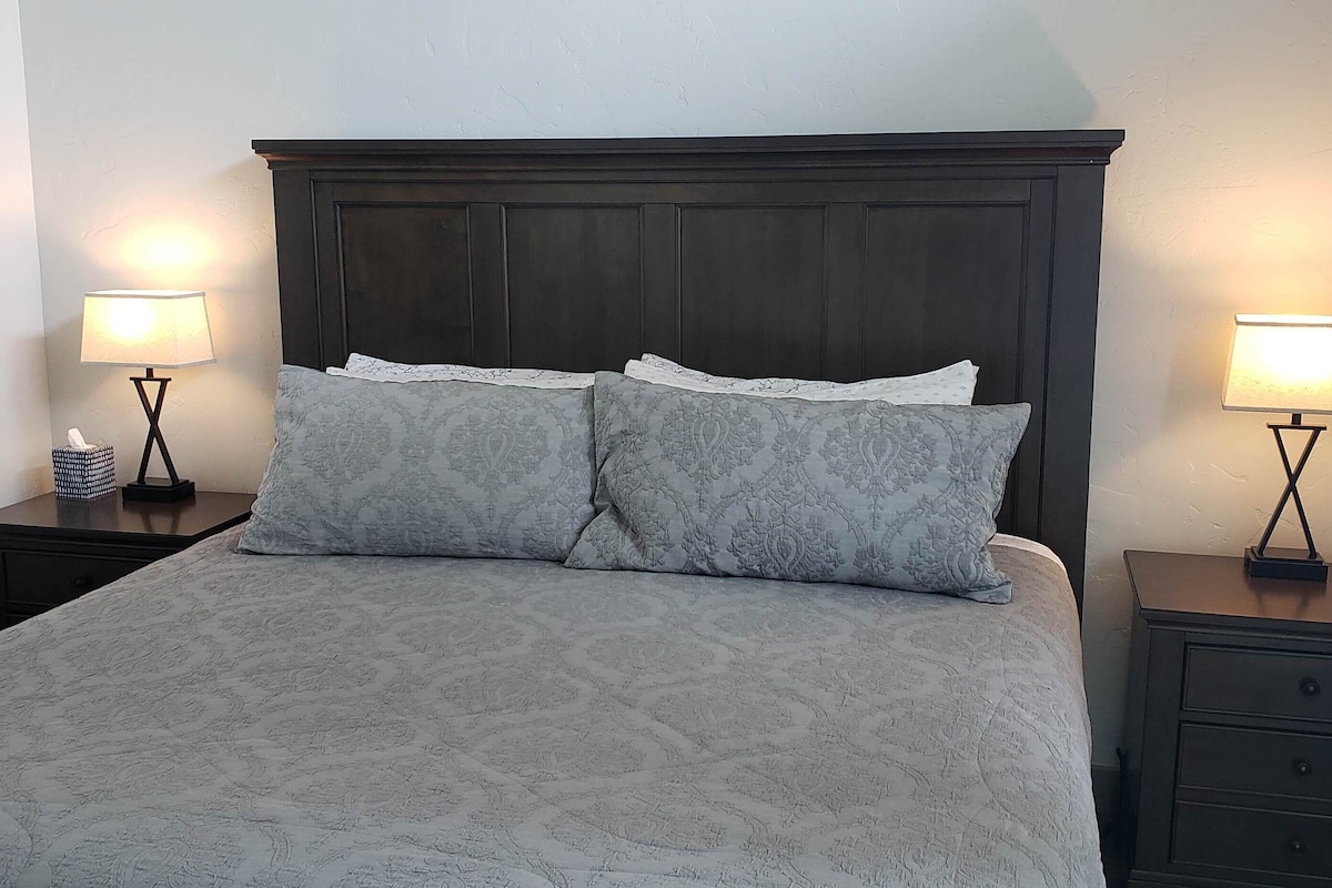 Un lit avec une tête de lit sombre, deux tables de chevet avec des lampes et une couvre-lit à motifs.