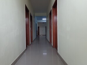A long, narrow hallway with wooden doors on both sides and a tiled floor. - Hotel Akash Palace (Noida)