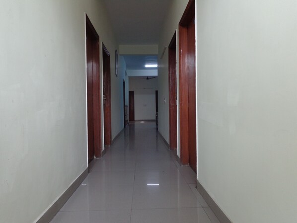 A long, narrow hallway with wooden doors on both sides and a tiled floor. - Hotel Akash Palace (Noida)