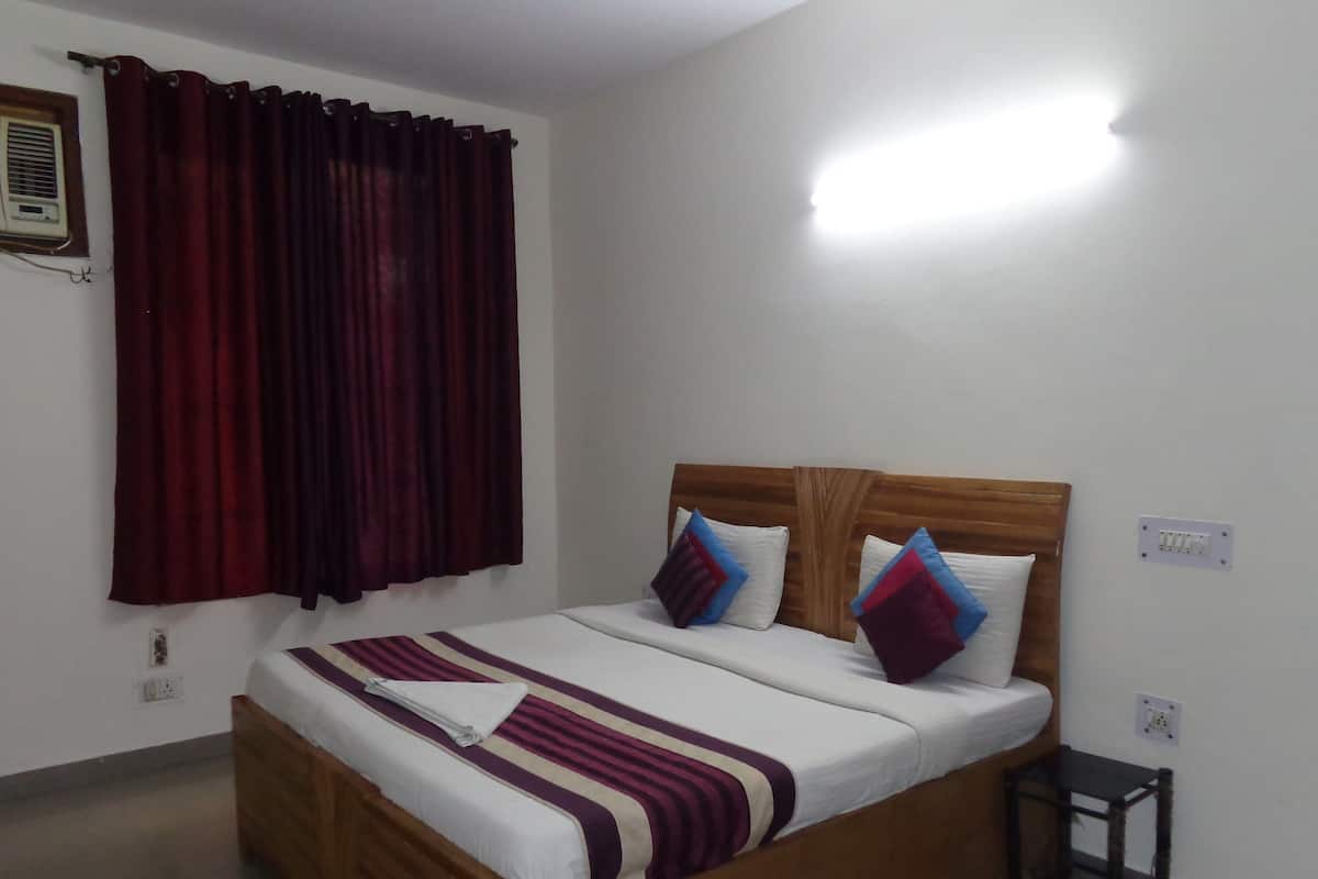 A neatly made bed with a wooden headboard, a bedside table, and a window with curtains.