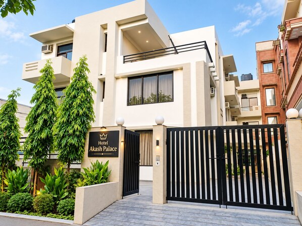 A modern hotel entrance with a gated driveway, a signboard, and lush greenery. - Hotel Akash Palace (Noida)
