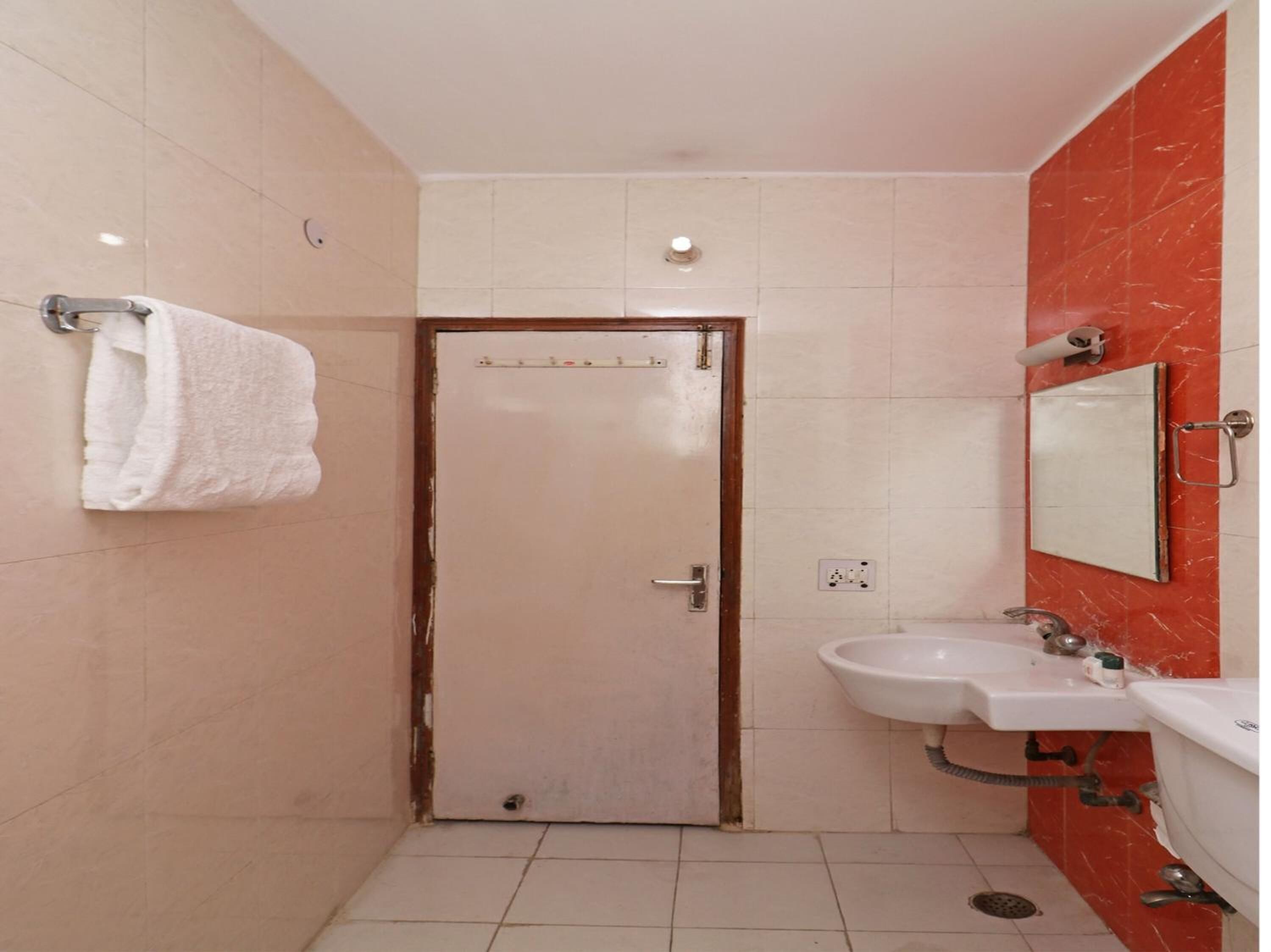 A bathroom with a white door, a sink with a mirror, and a towel hanging on a rack.