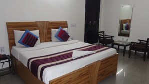 Una cama bien hecha con tablero de madera, dos almohadas, una colcha a rayas y una mesita de noche con una lámpara.