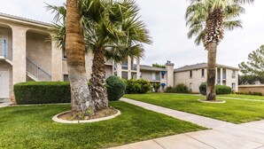 A residential building with a well-maintained lawn, palm trees, and a clear sky.
