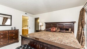 A bedroom with a large bed, a dresser, a nightstand, and a mirror.