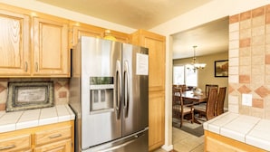 A kitchen with wooden cabinets, a stainless steel refrigerator, and a dining area with a chandelier.