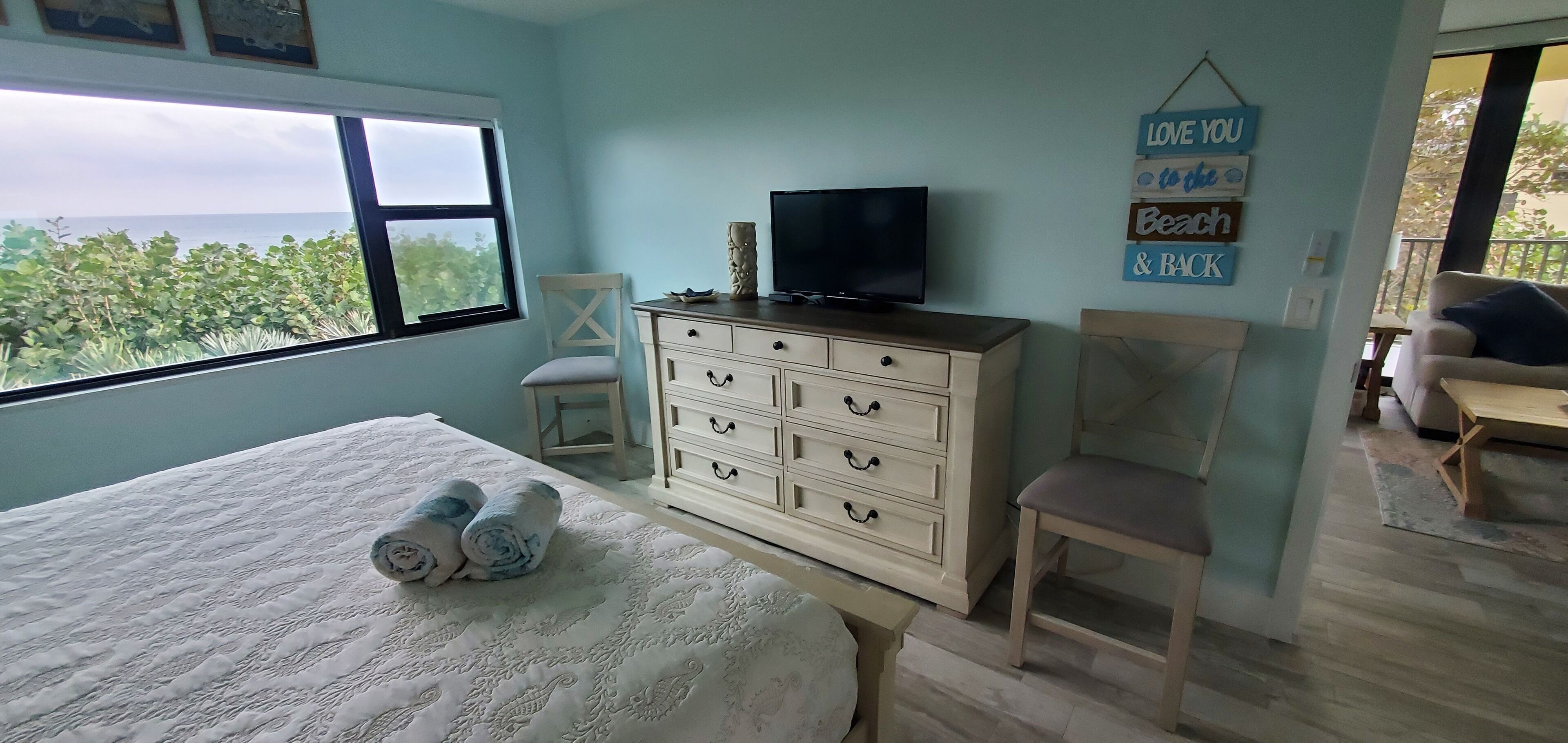 A bedroom with a bed, a dresser, a television, and a window with a view of greenery.