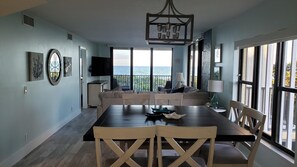Uma sala de jantar com uma mesa grande, cadeiras, uma televisão e vista para o oceano.