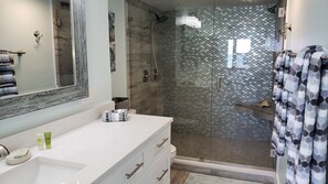 A modern bathroom with a glass shower enclosure, a white vanity with a mirror, and a towel rack with patterned towels.