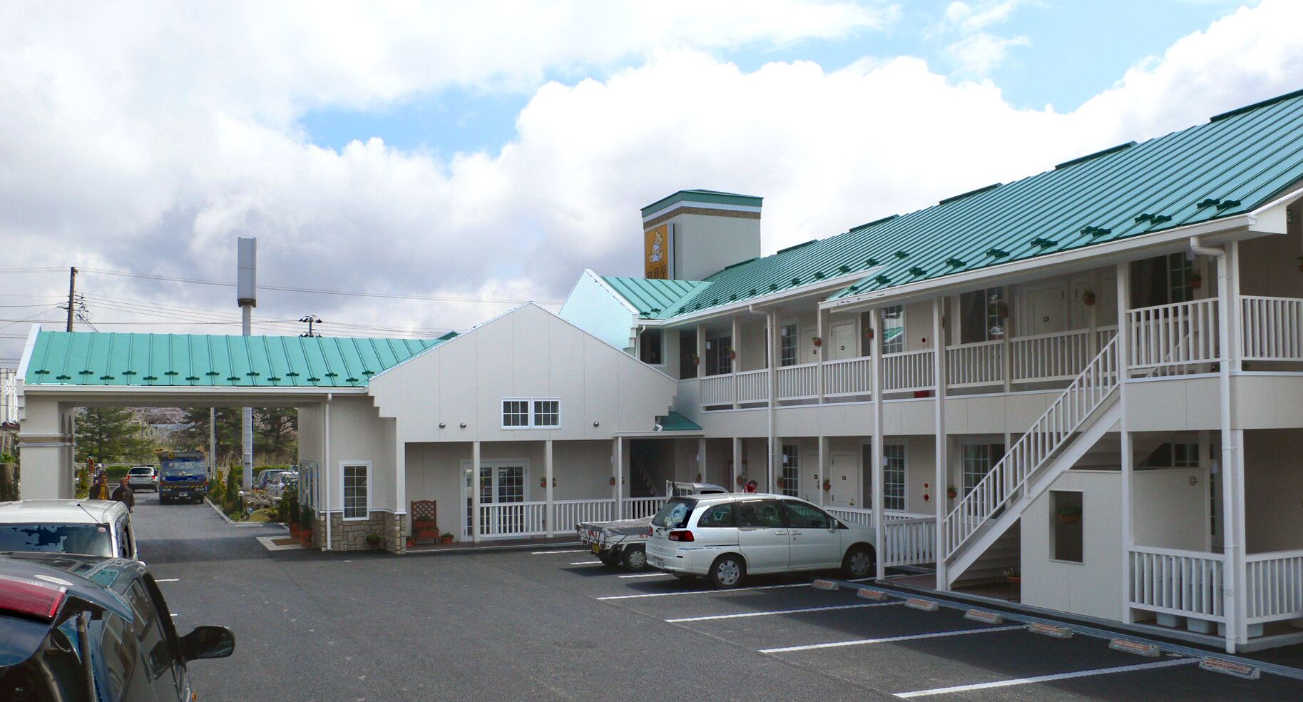 A two-story motel with a green roof, a covered parking area, and a white exterior.