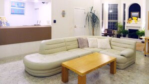 A living room with a beige sectional sofa, a wooden coffee table, and a reception desk with framed pictures. - Family Lodge Hatagoya Chiba Katsuura (Katsuura)