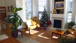 Uma sala de estar acolhedora com um urso de pelúcia grande, um pinheiro de Natal e uma lareira.