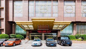 Ein Hotel Eingang mit modernem Design, der durch einen großen Vordach und ein Schild gekennzeichnet ist. Vor dem Gebäude sind mehrere Autos geparkt, und die Fassade ist symmetrisch mit großen Fenstern und einer Ziegelaußenwand.