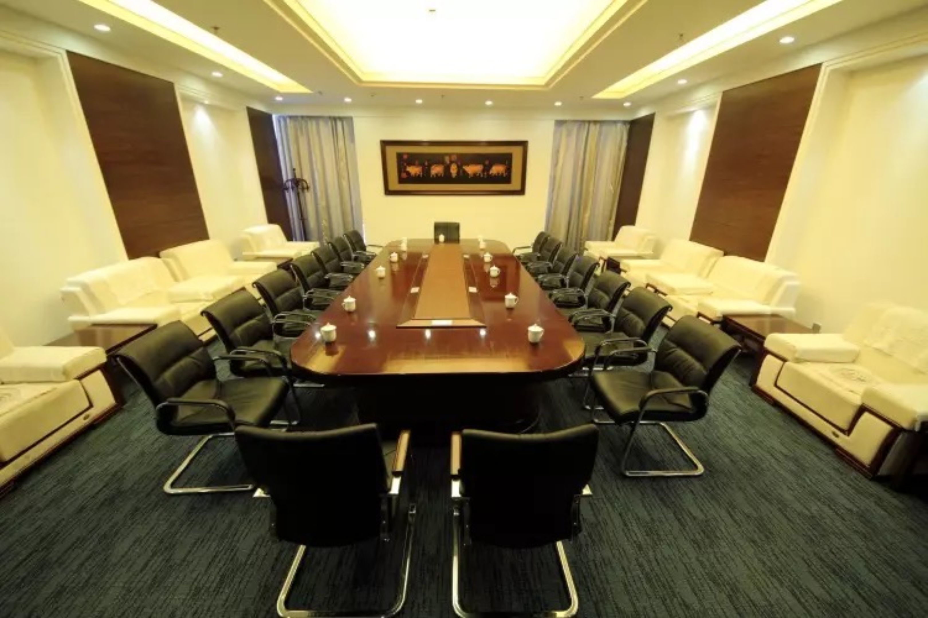 A conference room with a long table, black chairs, and white sofas.