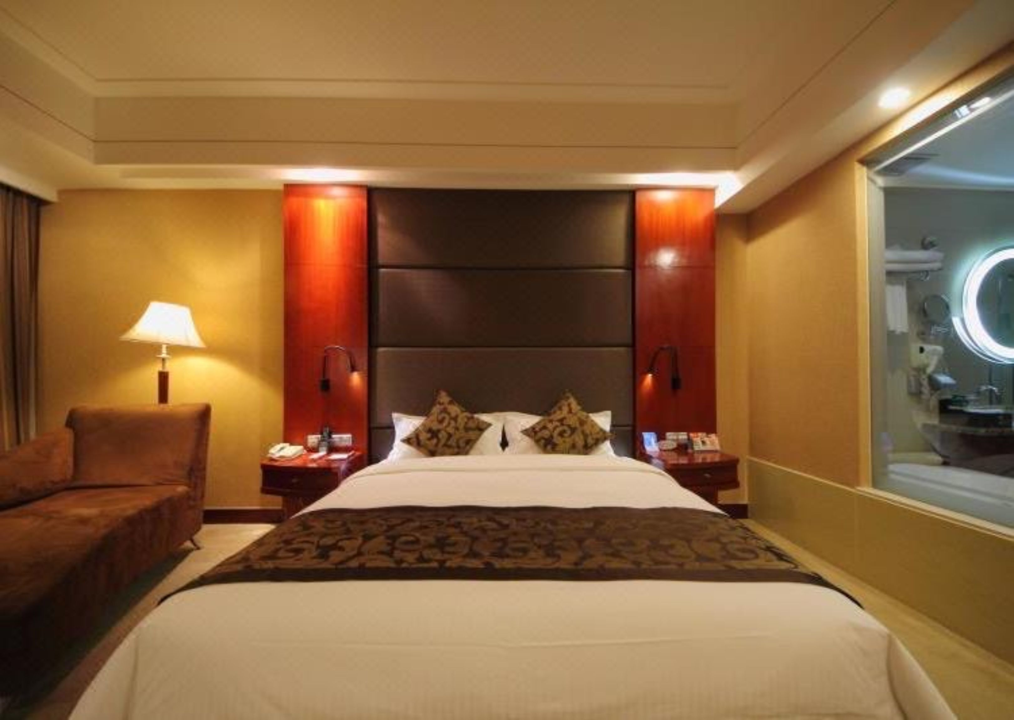 Una habitación de hotel con una cama grande, una mesita de noche, una lámpara y un espejo.