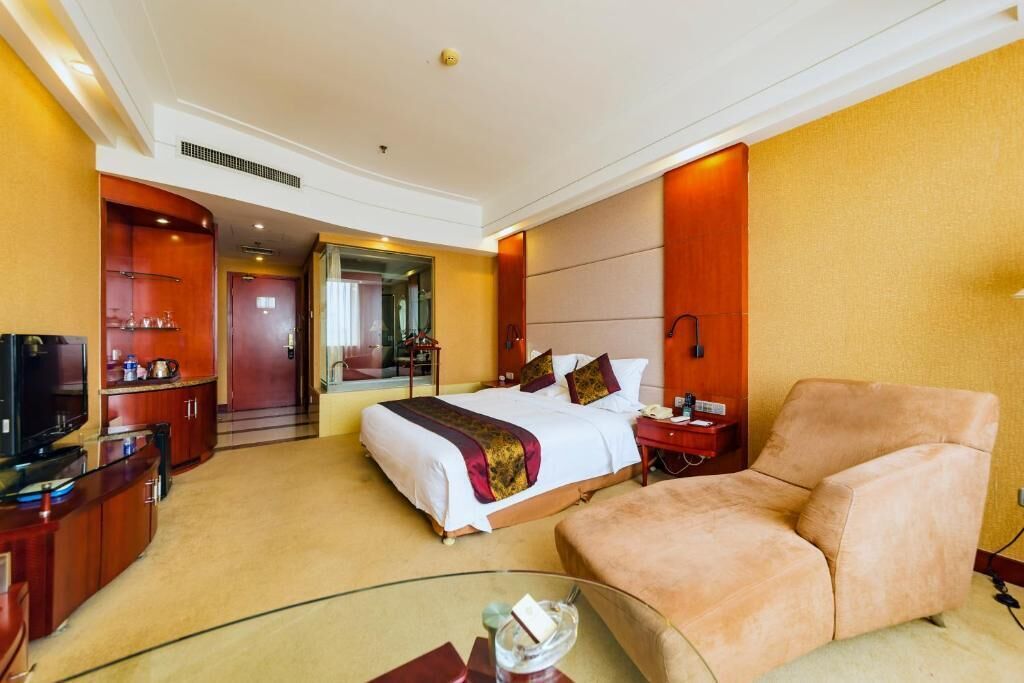 Habitación de hotel con una cama grande, televisión, una mesa de centro de vidrio y zona de estar.