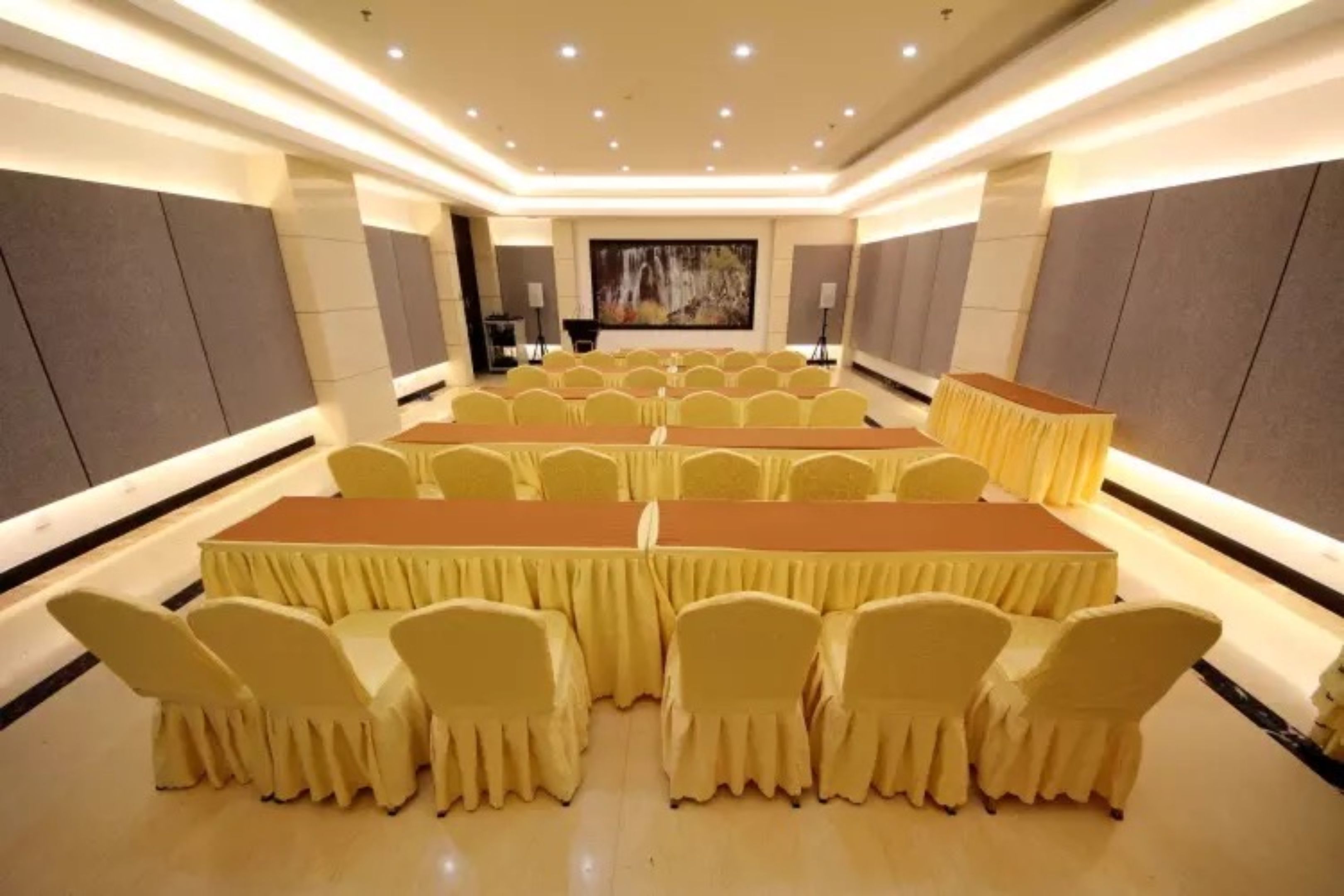 A conference room with rows of tables and chairs, a stage, and a large painting on the back wall.