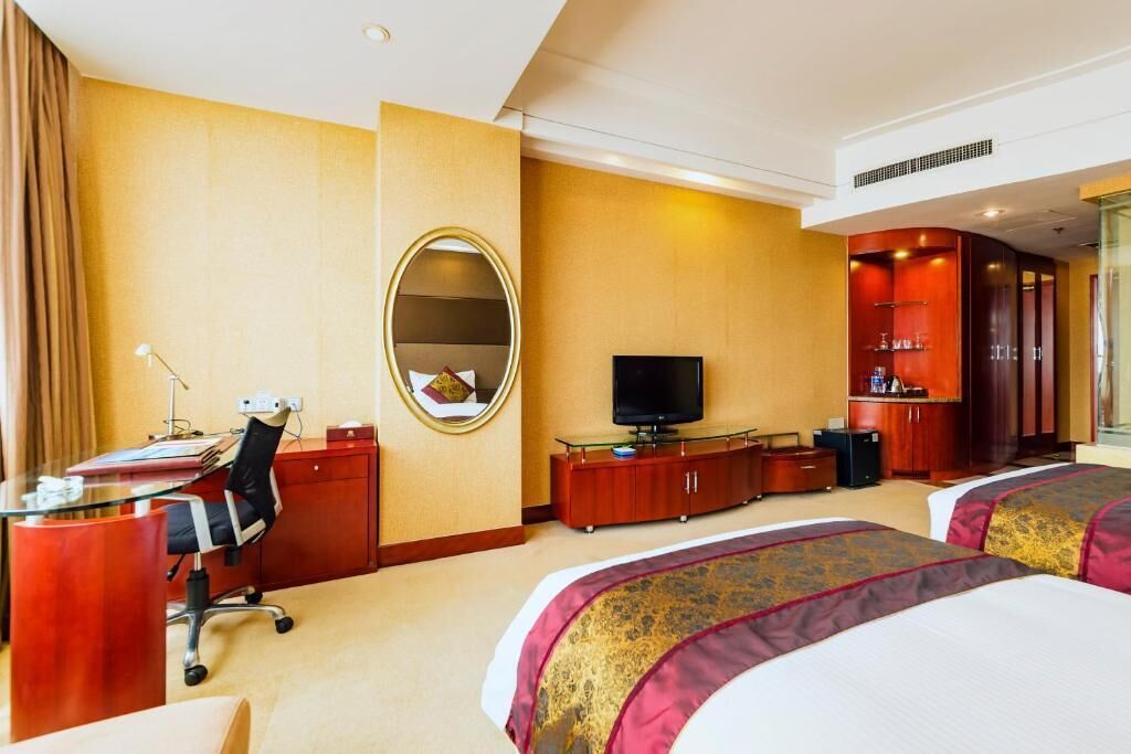 A hotel room with two beds, a desk with a chair, a television, a mirror, and a minibar.