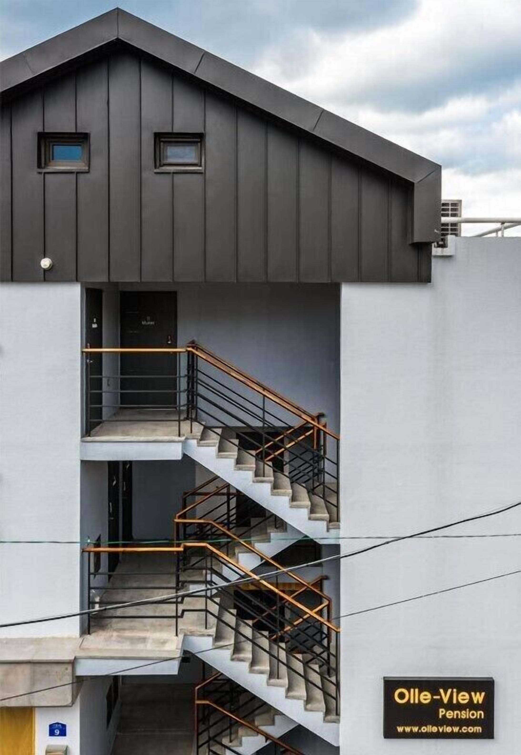 Um edifício moderno com fachada cinzenta, uma escadaria com corrimão de metal e uma pequena janela no andar superior.