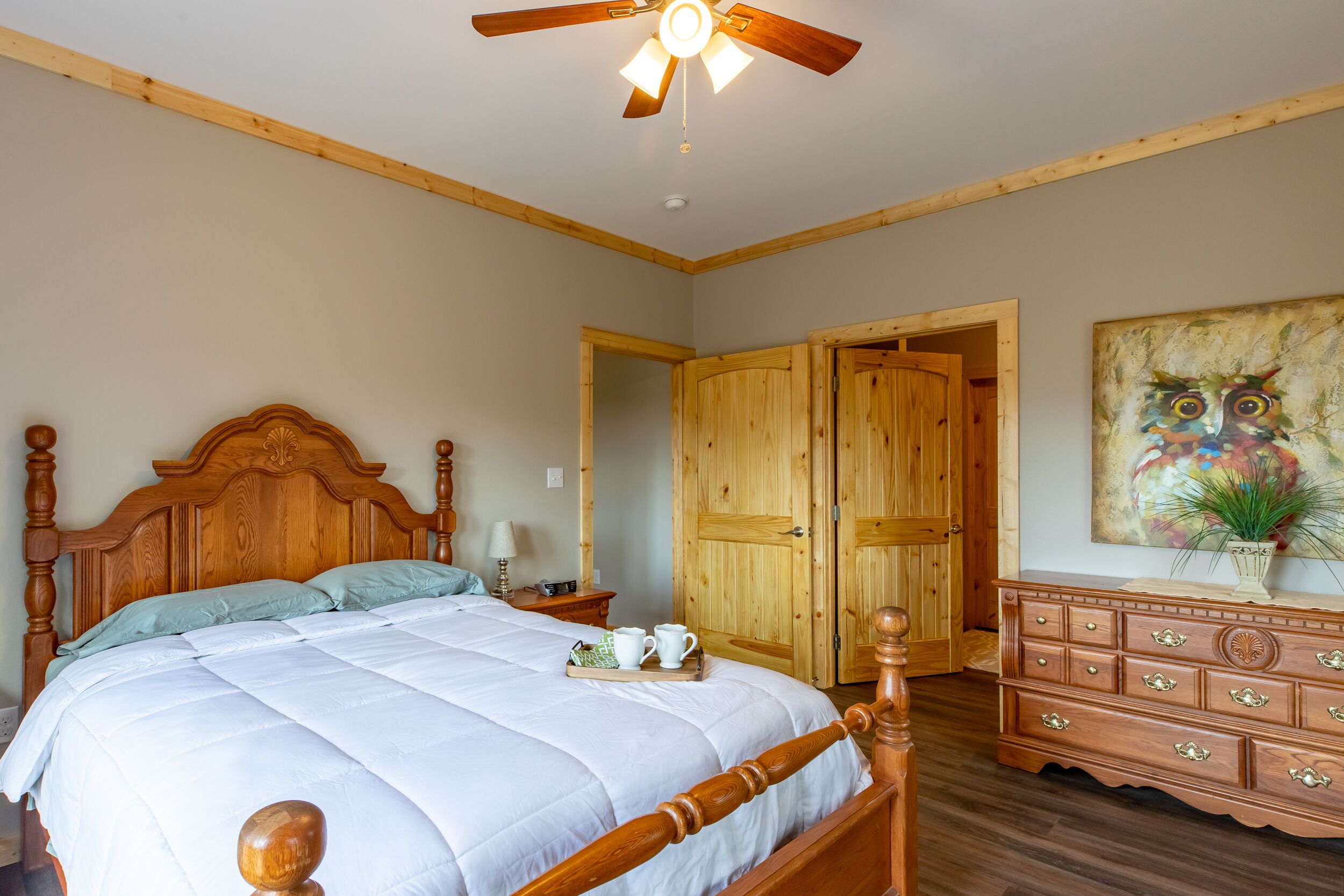Ein Schlafzimmer mit einem hölzernen Bett, einem Deckenventilator, einer Holzkommode und einem Bild an der Wand.