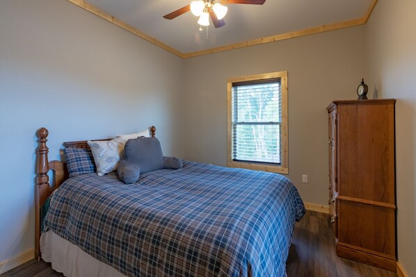 A bedroom with a bed, a wooden wardrobe, a window with blinds, and a ceiling fan.