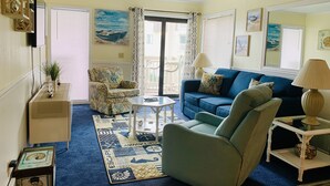 A living room with a blue sofa, a patterned armchair, a small table, and a decorative rug. - Beautiful beach Condo with ocean and pool view, very family oriented.  (Myrtle Beach)