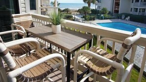 A balcony with a wooden table and chairs, a potted plant, and a view of a swimming pool and beach. - Beautiful beach Condo with ocean and pool view, very family oriented.  (Myrtle Beach)