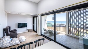 A modern living room with a large TV, comfortable seating, and a balcony with a view of the ocean. - Modeul Spa Pension (Seogwipo)