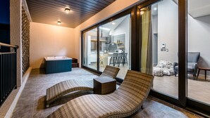 A balcony with wicker lounge chairs, a hot tub, and a view of a modern kitchen and living area. - Modeul Spa Pension (Seogwipo)