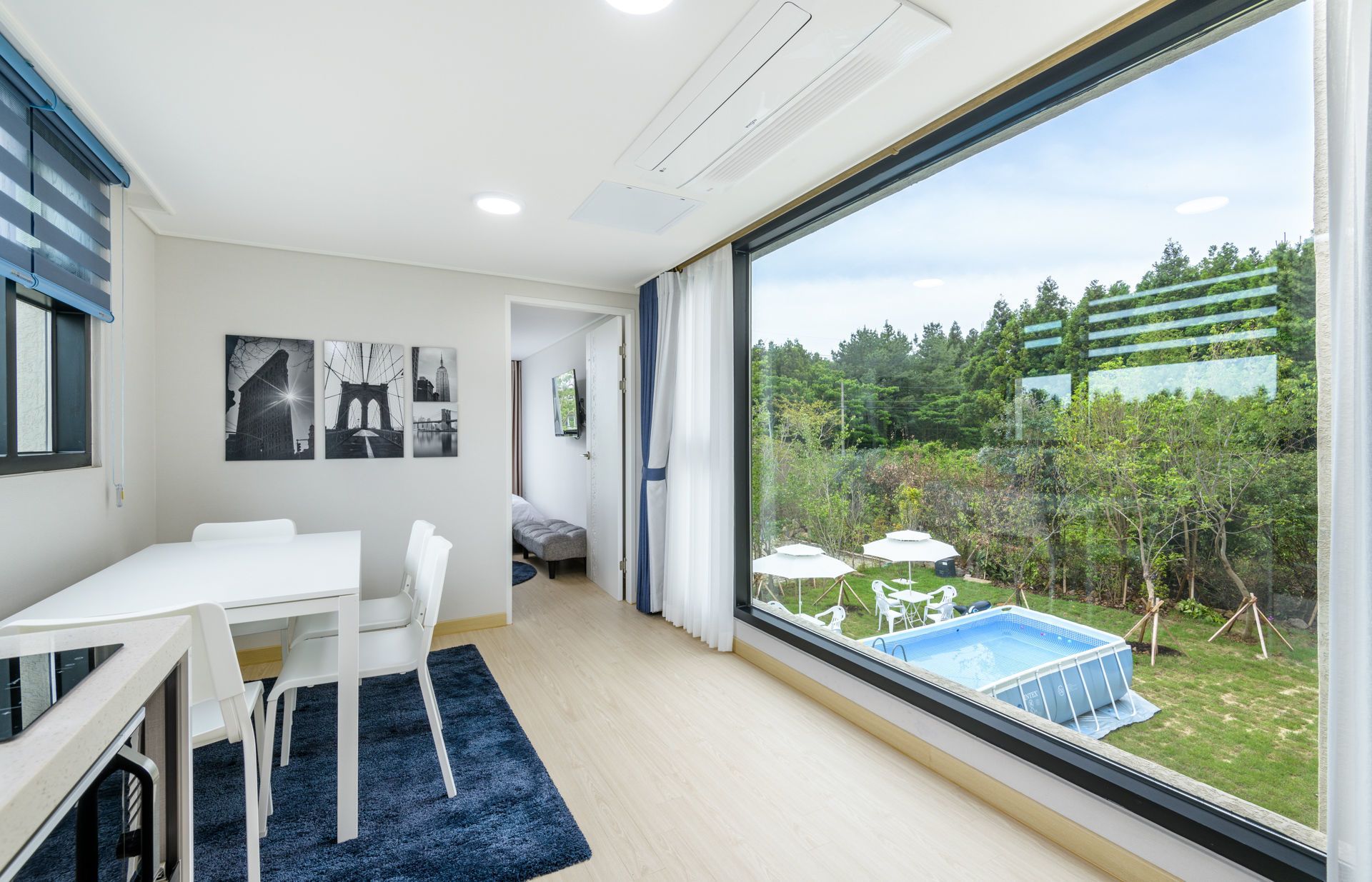 Quarto moderno com uma janela grande, área de refeições e vista para uma piscina e jardim.
